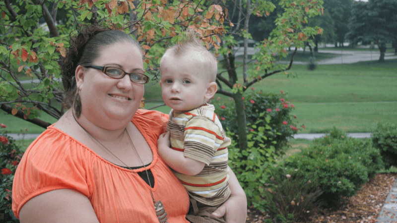 Mom holding toddler boy outside and smiling at the camera