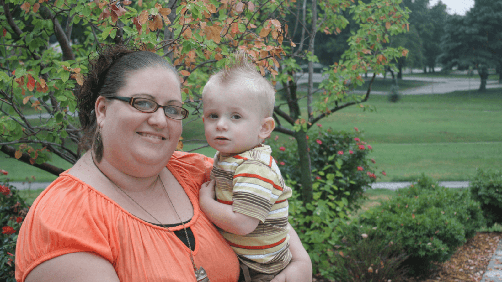 Mom holding toddler boy outside and smiling at the camera