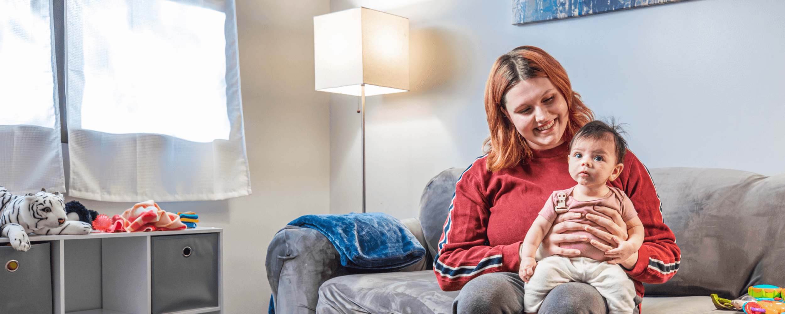 Young mom holding a baby on her knee while looking down and smiling at her